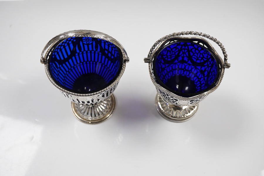 Two George III pierced silver pedestal sugar baskets, with blue glass liners, spiral handle, Burridge Davenport, London, 1777, the other William Plummer, London, 1775, tallest 10.1cm excluding the handle.